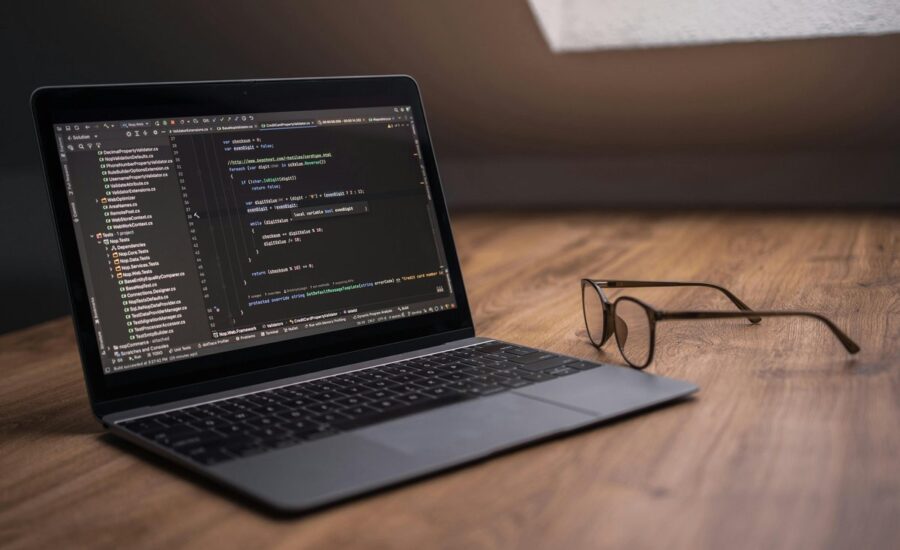 Laptop z otwartym edytorem kodu i okulary na drewnianym biurku